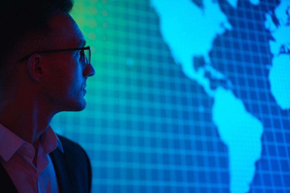 The businessman in glasses standing near big display